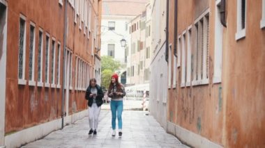 Sıcak giysiler içinde iki genç kadın gezginler dar sokaklarda yürüyüş ve konuşma
