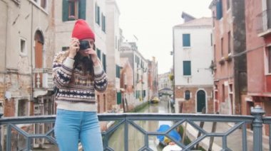Venedik su kanalı nın köprüsünde duran ve kamerasıyla fotoğraf çeken genç bir kadın