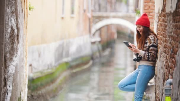 Una giovane donna ridente in piedi per le strade di Venezia e guardando lo schermo del suo telefono — Video Stock