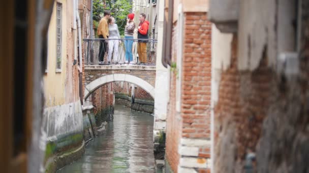 Um jovem amigo se reunindo em pé na ponte acima do canal de água e falando — Vídeo de Stock