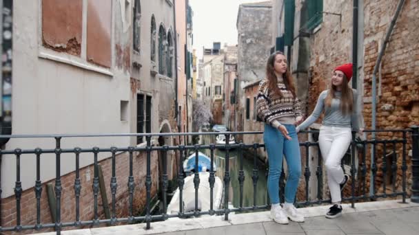 Italia, Veneţia. Două tinere călători stând pe podul mic peste canalul de apă și vorbind unul cu celălalt — Videoclip de stoc