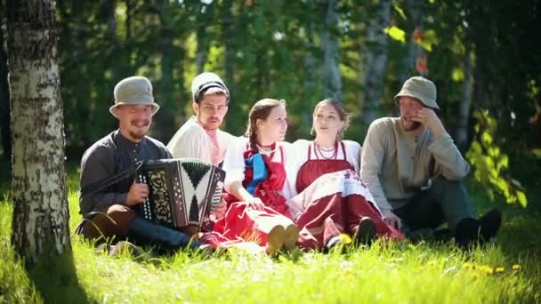 전통적인 러시아 옷을 입은 사람들은 잔디밭에 앉아 이야기를 나누다 — 비디오