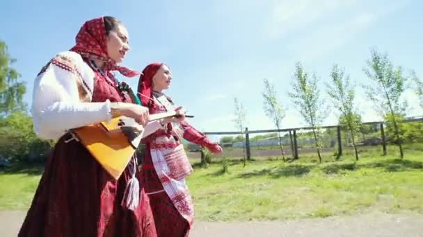 Dos mujeres jóvenes con ropa tradicional rusa caminando por la carretera en el pueblo — Vídeos de Stock