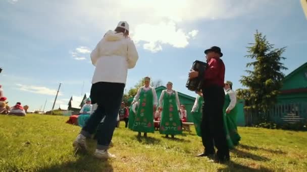 Rusya, Nikolskoe köyü, Tataristan Cumhuriyeti 25-05-2019: Geleneksel Rus kıyafetleri içinde yaşlı bir kadın sahada duruyor ve akordeon müziği yle dans ediyor chastooshkas — Stok video