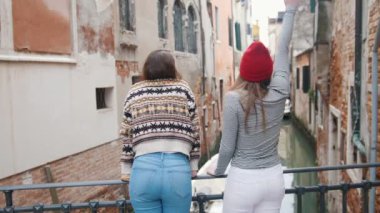 İki genç kadın gezginler bir su kanalı bir arka planda ayakta ve bunlardan biri eli ile sallayarak