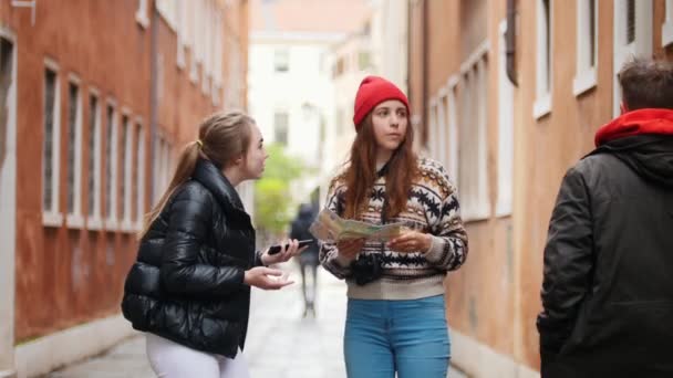 Дві молоді жінки стоять на вулиці і намагаються знайти шлях. Вони просять чоловіка допомогти їм за допомогою карти — стокове відео