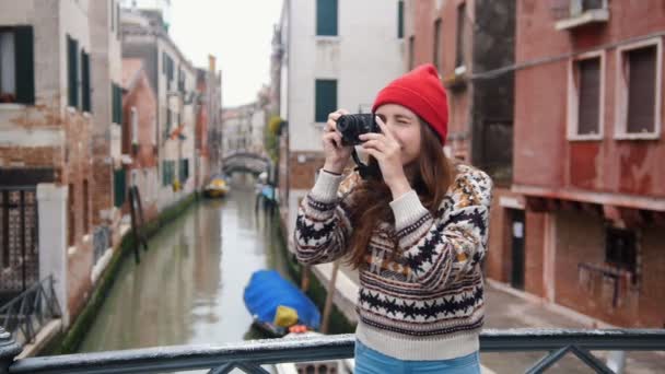 Jonge vrouw die op de brug staat op een achtergrond van een waterkanaal en een interessante foto maakt — Stockvideo