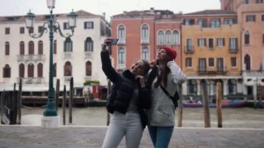 Bir kanalın arka planında duran ve selfie çeken iki genç gülümseyen kadın