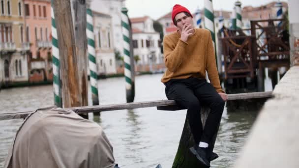 Een man zit op het bord boven het water en rookt — Stockvideo