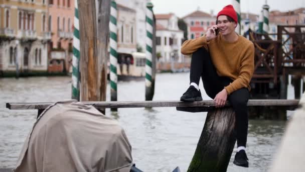 Un homme est assis sur la planche au-dessus de l'eau avec sa jambe suspendue et parlant au téléphone — Video