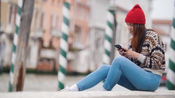 Young woman sits by the river and looking her phone — ストック動画