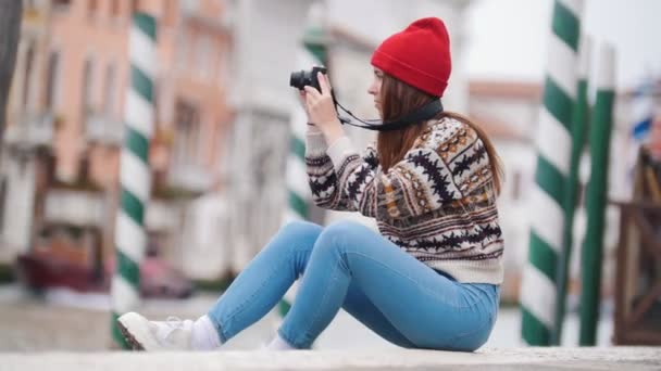 Young loughing woman sitting on concrete blocks near a river and takes pictures — Stock Video