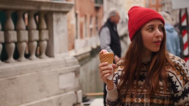 Jonge vrouw staan op een achtergrond van praten mensen en eet ijs. — Stockvideo