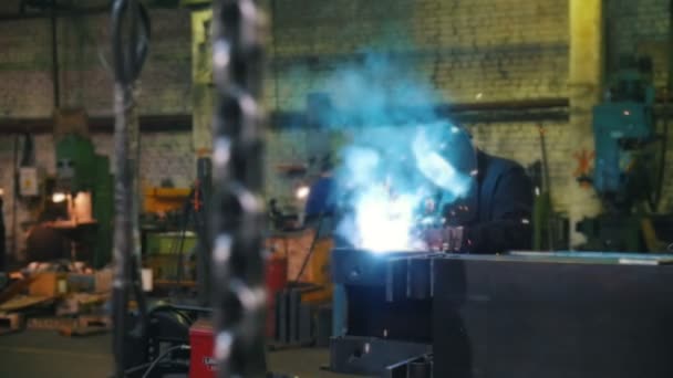 Fábrica de construção. Um homem de capacete usando uma máquina de solda. Uma corrente pendurada em primeiro plano — Vídeo de Stock