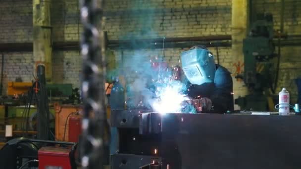 Bouw fabriek. Een man werknemer in een helm lassen Details. Een kettingen die op een voorgrond hangen — Stockvideo