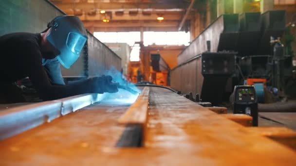 一名戴着防护面罩的男子坐在铁梁上, 通过焊接工作。焊接板在它的右边. — 图库视频影像