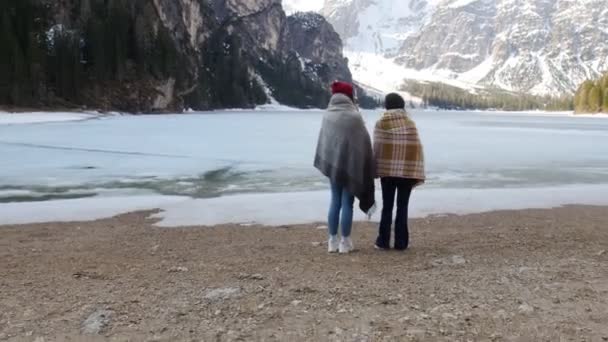 Két fiatal nő fedezi a takaró áll a fagyasztott tengerparton, és nézte a hegyeket — Stock videók