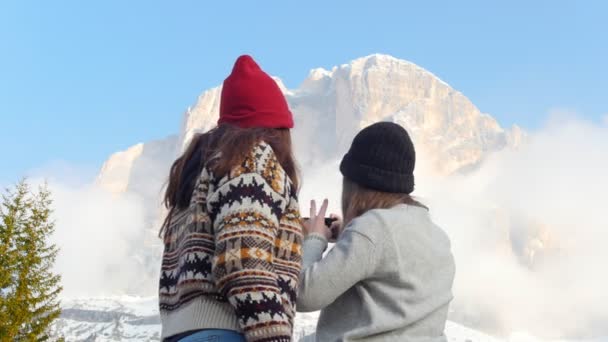 Två unga kvinnor som står på en bakgrund av ett molnigt berg och tar en selfie — Stockvideo
