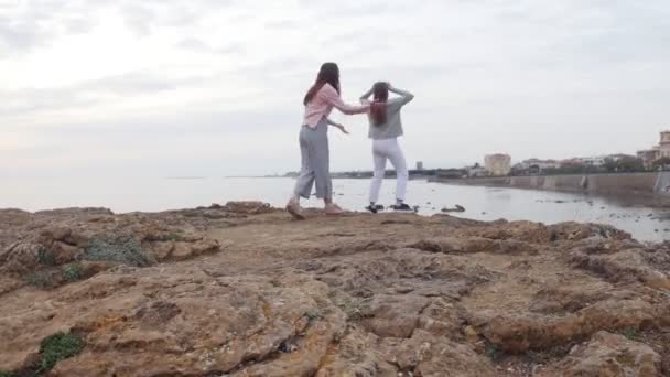 Zwei junge fröhliche Frauen, die fröhlich auf den Berg vor dem Hintergrund des Meeres springen — Stockvideo