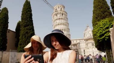 İtalya, Pisa. Pisa Kulesi 'nin bir arka planında duran ve selfie çeken iki genç gülümseyen kadın panamalar