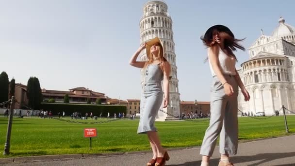 Włochy, Piza. Dwie młode kobiety w Panamas chodzenie na tle krzywej wieży w Pizy w jasny dzień — Wideo stockowe