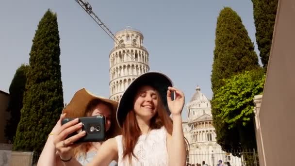 Италия, Пиза. Две молодые улыбающиеся женщины в панамах, стоящие на фоне Пизанской башни и делающие селфи — стоковое видео