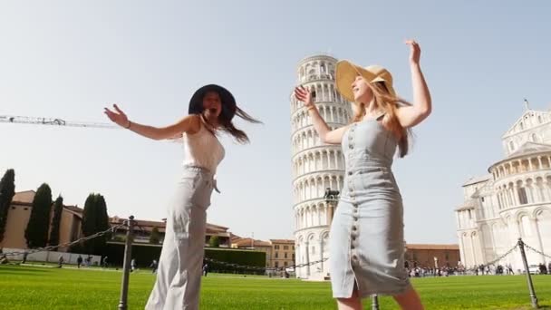 Italië, Pisa. Twee jonge gelukkige vrouwen in Panamas lopen op een achtergrond van de scheve toren van Pisa op een heldere dag — Stockvideo