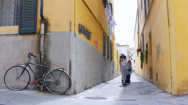 Două tinere care călătoresc fericite mergând cu un bagaj în jurul pereților galbeni — Videoclip de stoc