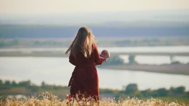 En kvinna leker med sin lilla bebis på fältet på en bakgrund av floden — Stockvideo