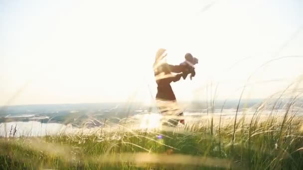 Jonge vrouw spelen met haar baby op de achtergrond van de zonsondergang — Stockvideo