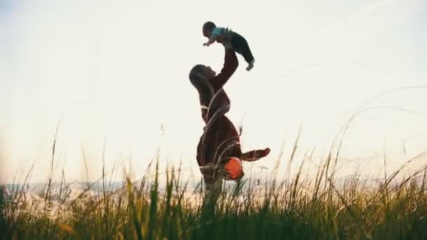 Ung kvinna kastar upp barnet och pratar med honom. På sommarfältet — Stockvideo