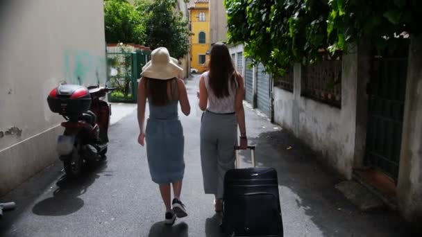 Dvě mladé ženy chodí přes ulice. Jeden z nich nosí kufr — Stock video