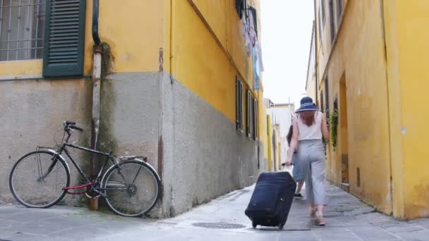 Twee vrouwen betreden het steegje en gaan rechtdoor. Een van hen draagt een koffer — Stockvideo