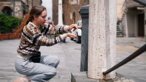 Una mujer viene a la torre de agua y se sienta. Vierte agua en la mano — Vídeo de stock