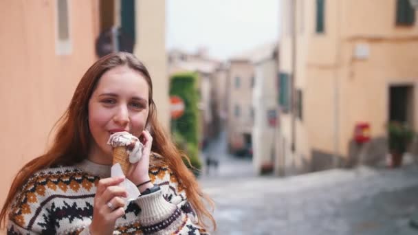 Молодая улыбающаяся женщина ест мороженое в городе — стоковое видео
