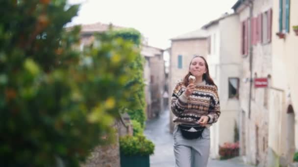 Genç gülümseyen kadın sokak boyunca yürür ve dondurma yiyor. — Stok video