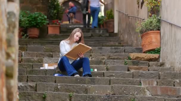 Young woman sits on the stairs and draws on canvas — Stock Video