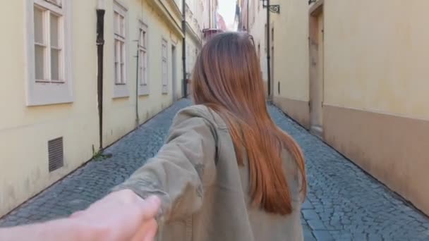 En ung leende kvinna som leder sin pojkvän kasta gatan för hand — Stockvideo