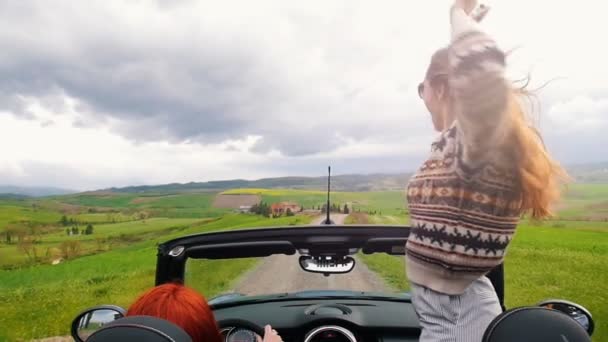 Zwei junge Frauen in einem Cabrio. einer von ihnen stand auf und winkte — Stockvideo