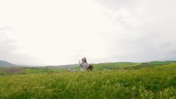 Молодая привлекательная женщина сидит посреди зеленого луга — стоковое видео