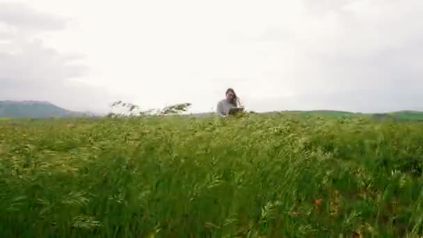 한 젊은 매력적인 여성이 언덕에 앉아 그림을 그립니다. 바람이 불고. — 비디오