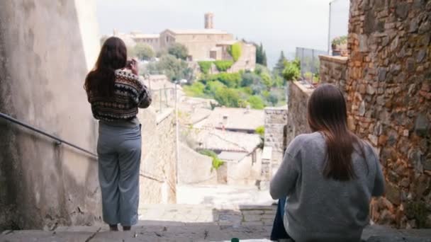 Dos mujeres jóvenes en las escaleras. Uno de ellos dibuja, y el otro fotografía el paisaje . — Vídeos de Stock