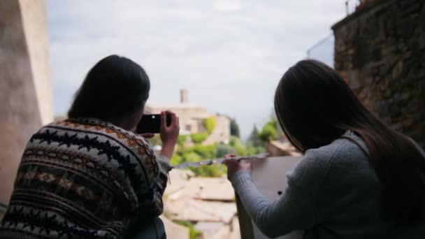 Дві жінки сидять біля сходів, одна з яких малює. Тоді інша жінка отримує фотоапарат . — стокове відео
