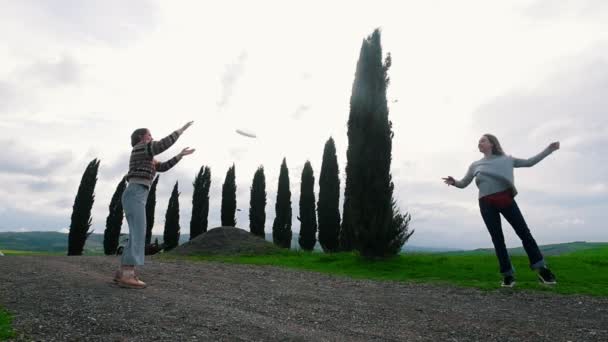 Dos atractivas mujeres lanzan un plato en un camino de grava en medio de un campo verde . — Vídeos de Stock