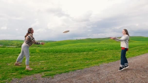 Dos mujeres riendo lanzando un plato sobre un fondo de paisaje verde — Vídeos de Stock