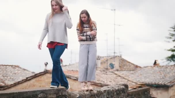 Twee jonge vrouwen lopen op een bakstenen hek — Stockvideo