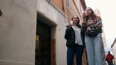 İki genç kadın sokakta durmak - kahve içmek ve gülmek