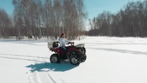 Mulher dirigindo ATV no campo de neve homem cavalga atrás dela — Vídeo de Stock