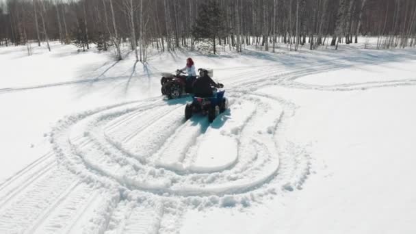 Uma mulher monta um quad em torno de um homem em um campo coberto de neve . — Vídeo de Stock