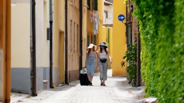 Dos mujeres jóvenes en panamas caminando por la calle con la maleta — Vídeos de Stock